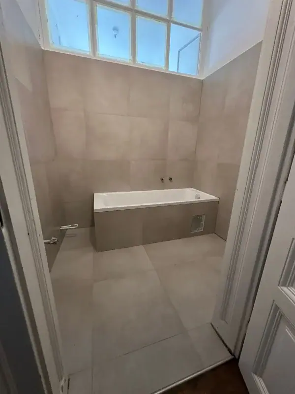 Bad mit Badewanne unter dem Fenster und großformatigen beigen Fliesen