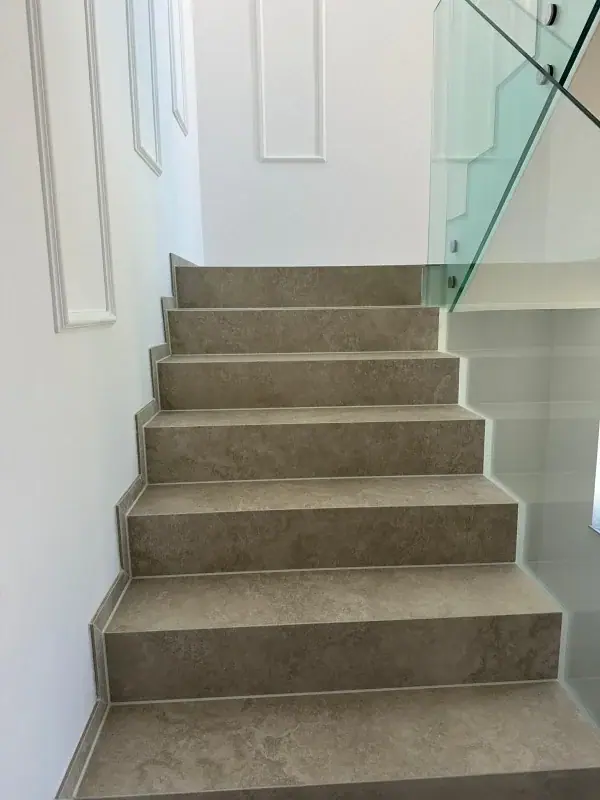 Stiege mit Fliesenstufen in Steinoptik und Glasgeländer