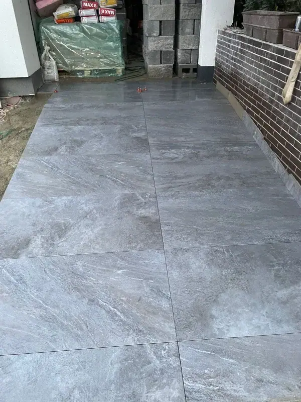 Außenfläche mit großformatigen Platten in Marmoroptik neben einer Klinkermauer
